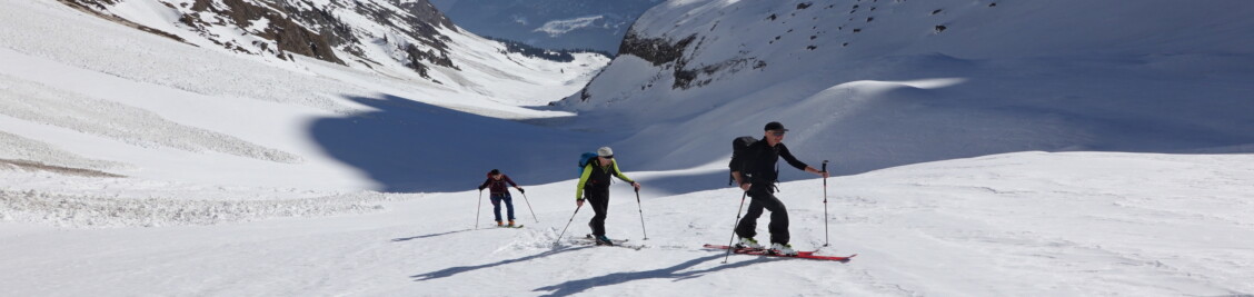 Drei Skitourenpersonen im Aufstieg in einem Tal